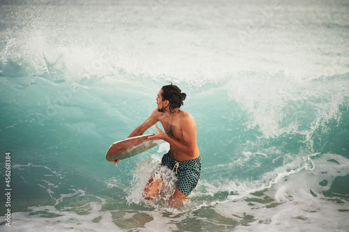 Man with skimboard running away from a big wave breaking against him