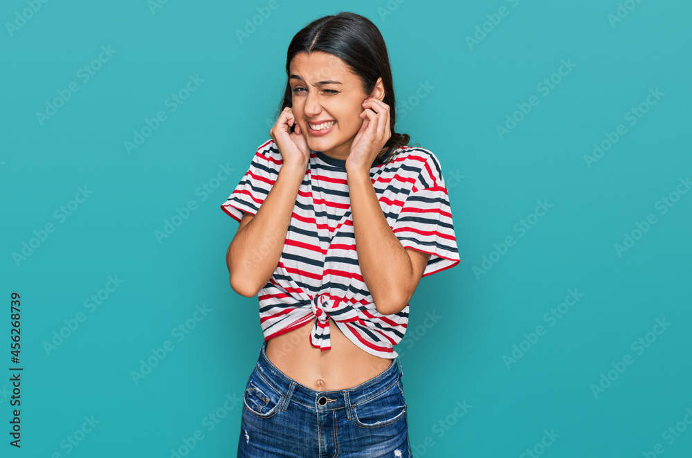 Young hispanic girl wearing casual clothes covering ears with fingers with annoyed expression for the noise of loud music. deaf concept. Young hispanic girl wearing casual clothes covering ears with fingers with annoyed expression for the noise of loud music. deaf concept.
