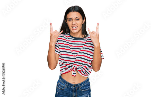 Young hispanic girl wearing casual clothes shouting with crazy expression doing rock symbol with hands up. music star. heavy concept.