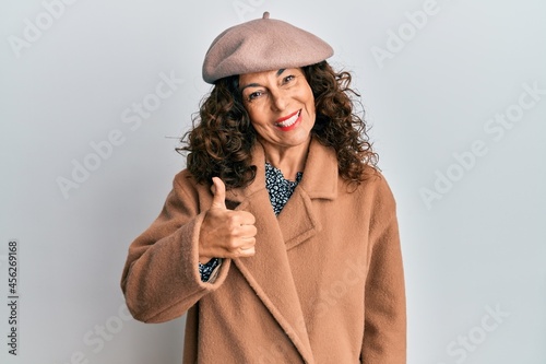 Middle age hispanic woman wearing french look with beret doing happy thumbs up gesture with hand. approving expression looking at the camera showing success.
