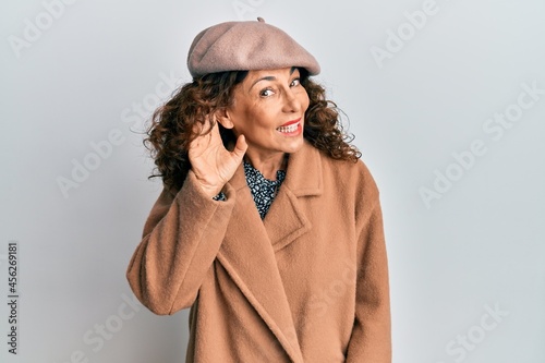 Middle age hispanic woman wearing french look with beret smiling with hand over ear listening an hearing to rumor or gossip. deafness concept.