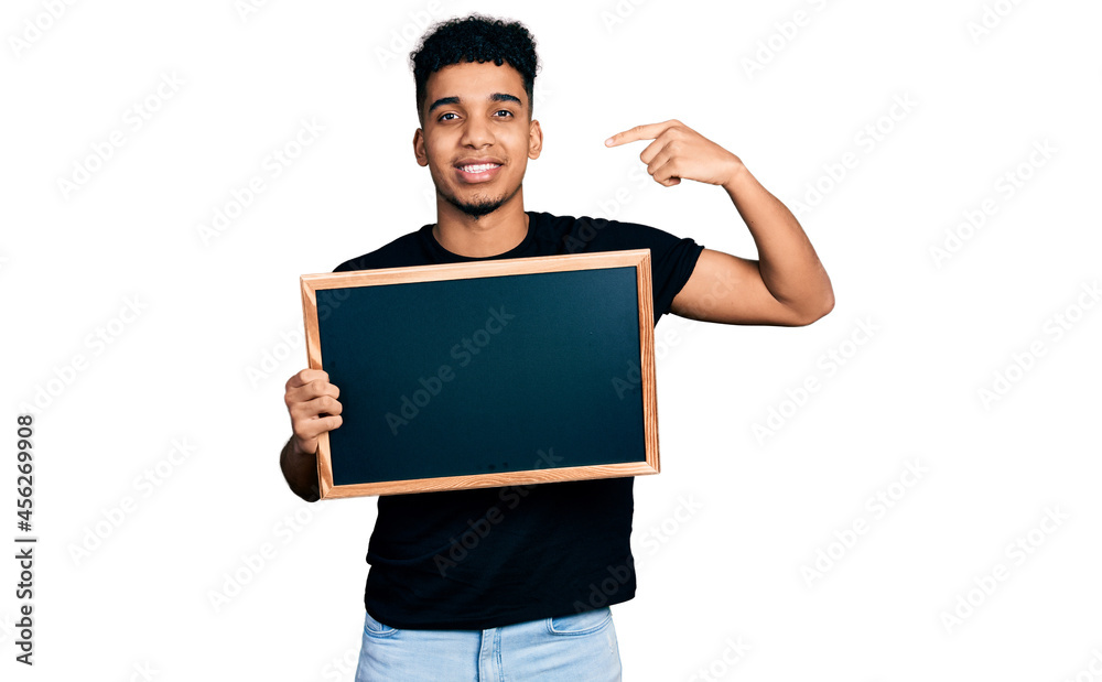 Young african american man holding blackboard pointing finger to one self smiling happy and proud Young african american man holding blackboard pointing finger to one self smiling happy and proud