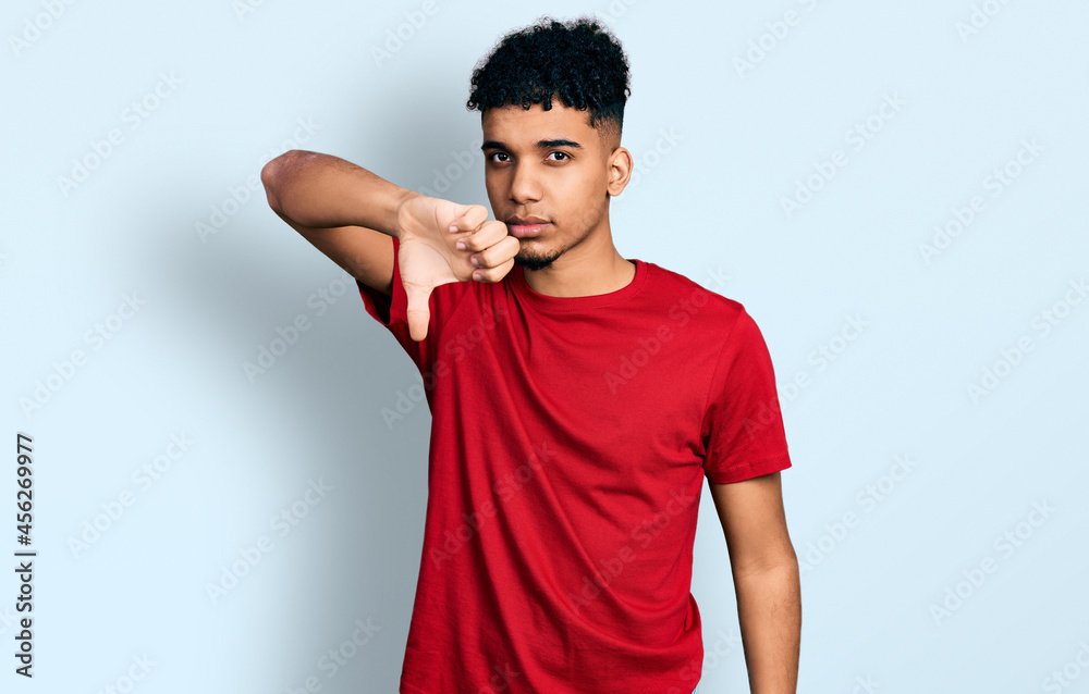 Young african american man wearing casual red t shirt looking unhappy and angry showing rejection and negative with thumbs down gesture. bad expression. Young african american man wearing casual red t shirt looking unhappy and angry showing rejection and negative with thumbs down gesture. bad expression.
