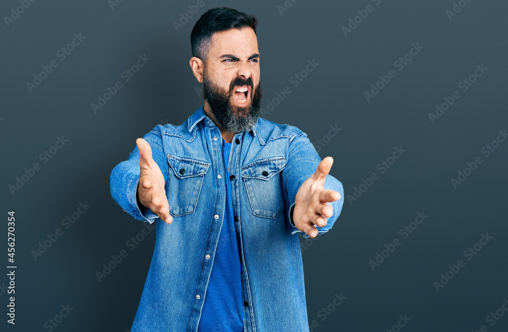 Hispanic man with beard with open arms doing hug gesture angry and mad ...