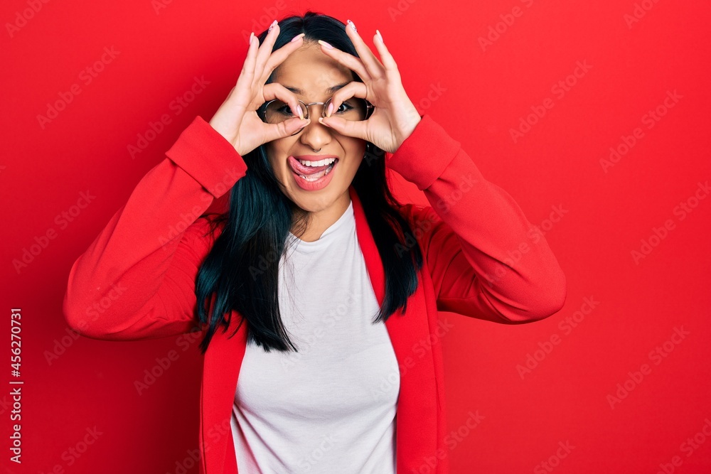 Beautiful hispanic woman with nose piercing wearing casual look and glasses doing ok gesture like binoculars sticking tongue out, eyes looking through fingers. crazy expression.