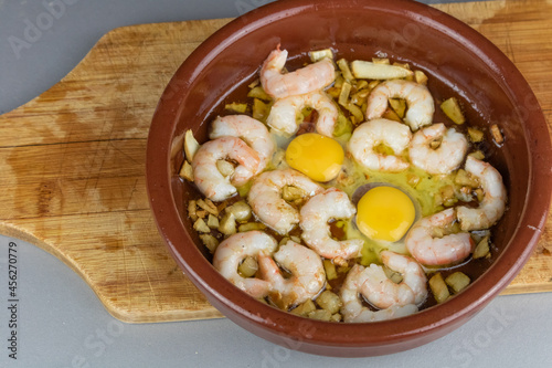 Shrimps or prawns in garlic olive oil in a crock pot, spanish appetizer on a wooden board. Typical spanish tapa. Dark rustic style food. Gambas al ajillo.