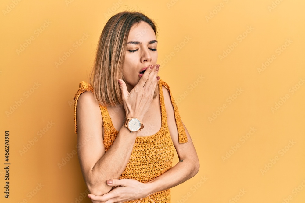 Young caucasian blonde woman wearing casual yellow t shirt bored yawning tired covering mouth with hand. restless and sleepiness.