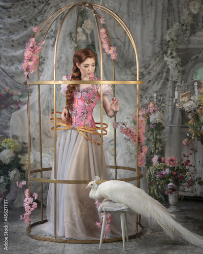 Red-haired girl in a golden cage with a white peacock photo