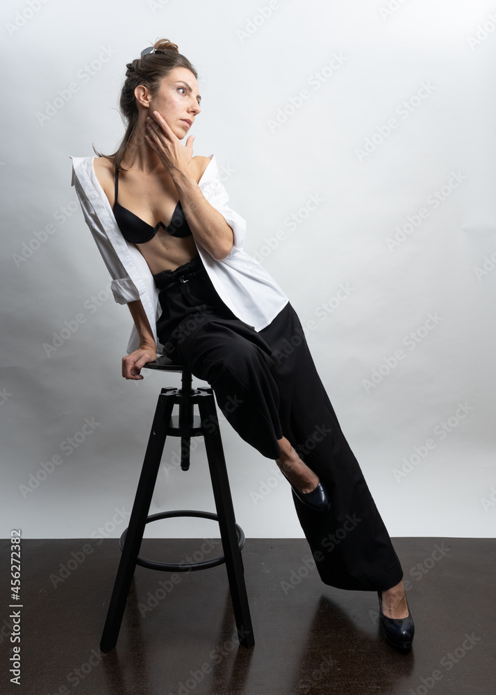 Model, brunette posing on a white background in the studio. She is wearing a white shirt, a black hairstyle. Photo to the waist
