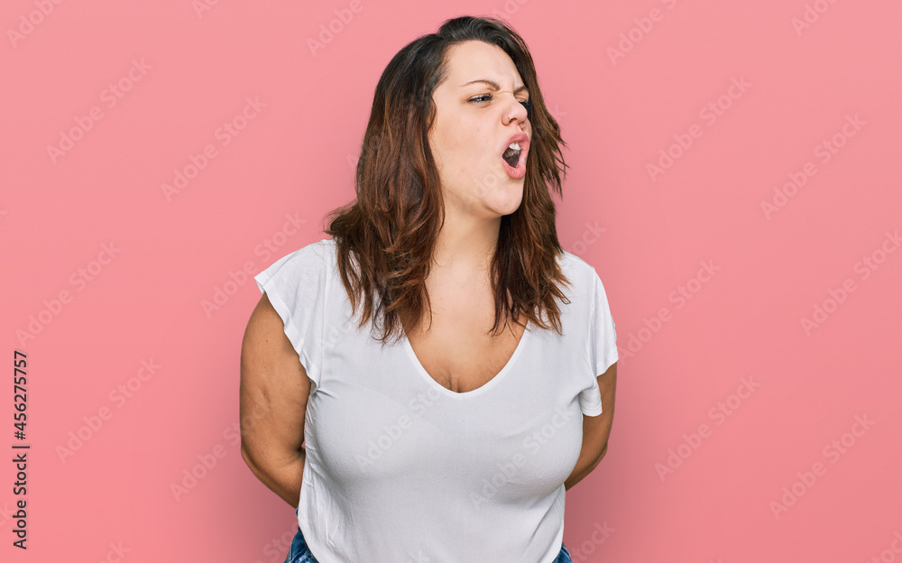 Young plus size woman wearing casual white t shirt angry and mad screaming frustrated and furious, shouting with anger. rage and aggressive concept.