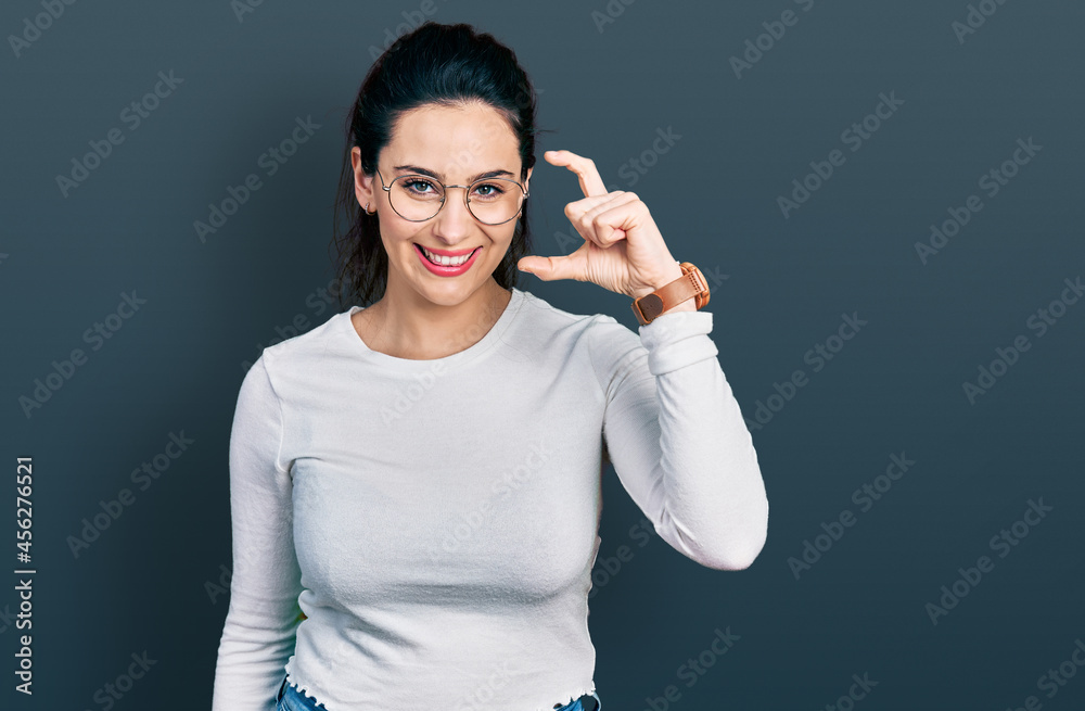 Young hispanic woman wearing casual clothes smiling and confident gesturing with hand doing small size sign with fingers looking and the camera. measure concept. Young hispanic woman wearing casual clothes smiling and confident gesturing with hand doing small size sign with fingers looking and the camera. measure concept.