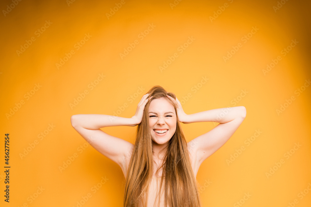 An attractive girl with long hair smiles broadly and holds her head with both hands on an orange background An attractive girl with long hair smiles broadly and holds her head with both hands on an orange background