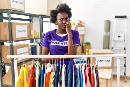 African young woman wearing volunteer t shirt at donations stand looking stressed and nervous with hands on mouth biting nails. anxiety problem.