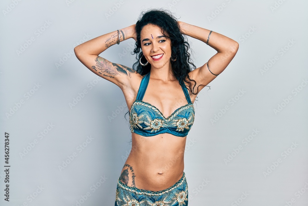 Fototapeta premium Young woman wearing bindi and traditional belly dance clothes relaxing and stretching, arms and hands behind head and neck smiling happy
