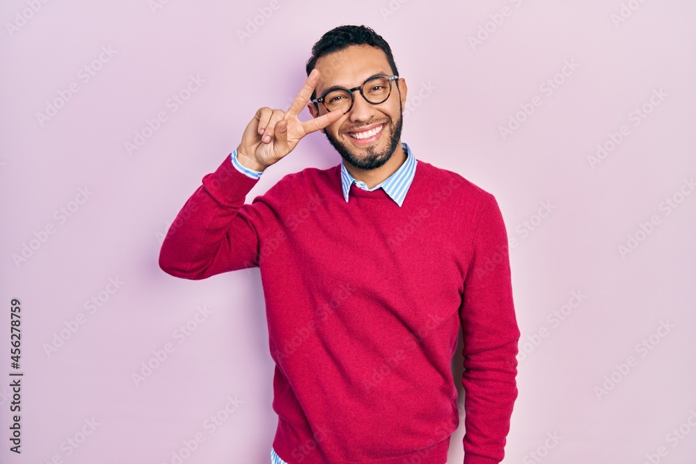 Hispanic man with beard wearing business shirt and glasses doing peace symbol with fingers over face, smiling cheerful showing victory Hispanic man with beard wearing business shirt and glasses doing peace symbol with fingers over face, smiling cheerful showing victory