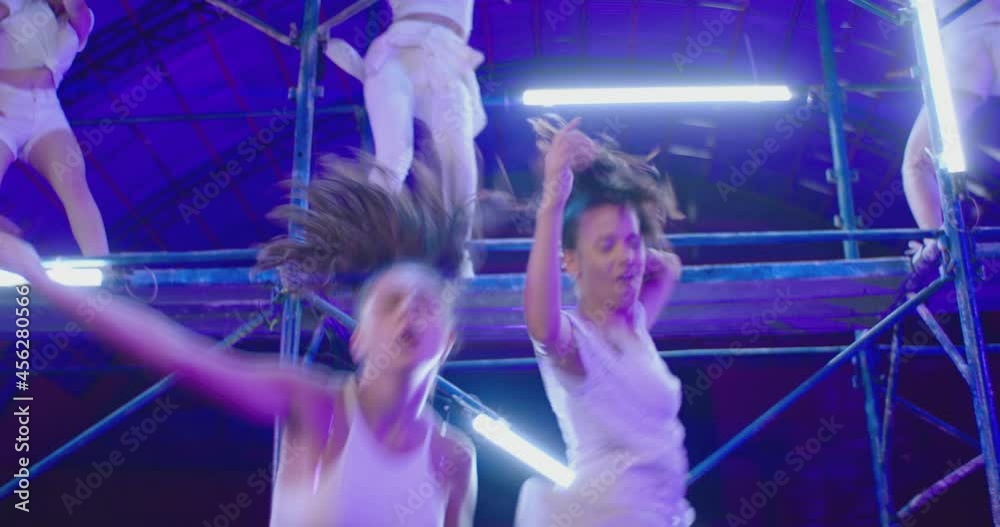 Many female dancers dressed in white shorts dancing inside abandoned