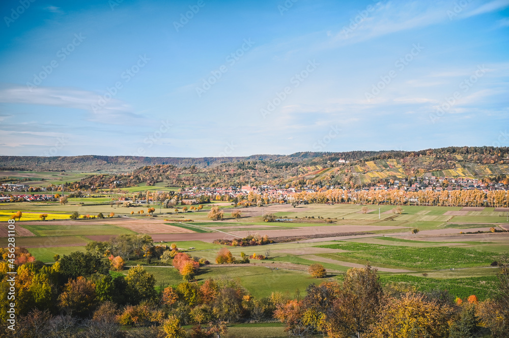 Panoramic view of an autumnal countryside: colorful meadows and trees, fields and forested hills of the Schönbuch natural reserve in the background.