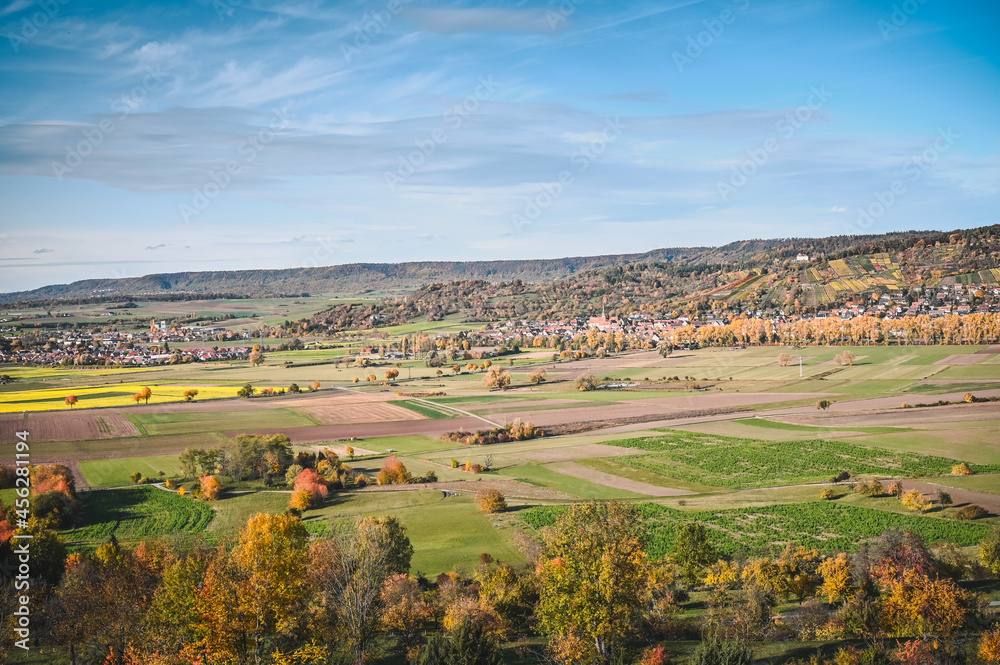 Panoramic view of an autumnal countryside: colorful meadows and trees, fields and forested hills of the Schönbuch natural reserve in the background.