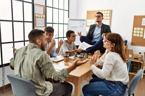 Businessman enjoys meditating during meeting. Sitting on desk near arguing partners at the office.