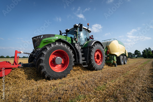 Strohernte - Traktor mit moderner Hochdruckpresse beim Pressen von Strohballen in Quaderform.