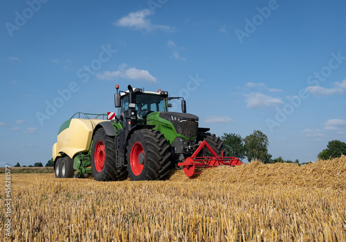 Strohernte - Traktor mit moderner Hochdruckpresse beim Pressen von Strohballen in Quaderform.