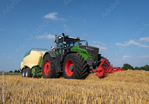 Strohernte - Traktor mit moderner Hochdruckpresse beim Pressen von Strohballen in Quaderform.