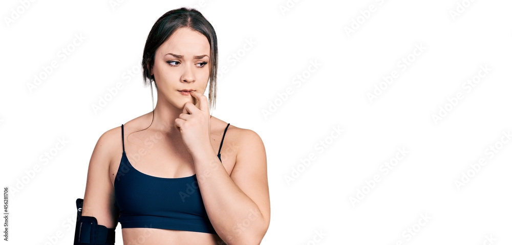 Young hispanic woman wearing sportswear looking stressed and nervous with hands on mouth biting nails. anxiety problem. Young hispanic woman wearing sportswear looking stressed and nervous with hands on mouth biting nails. anxiety problem.