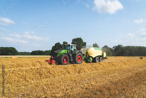 Strohernte - Traktor mit moderner Hochdruckpresse beim Pressen von Strohballen in Quaderform.