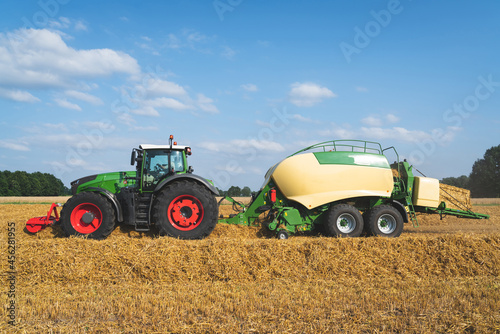 Strohernte - Traktor mit moderner Hochdruckpresse beim Pressen von Strohballen in Quaderform.