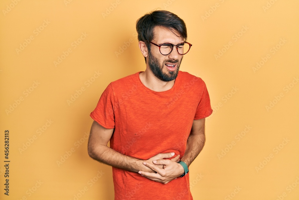 Young hispanic man wearing casual clothes and glasses with hand on stomach because nausea, painful disease feeling unwell. ache concept. Young hispanic man wearing casual clothes and glasses with hand on stomach because nausea, painful disease feeling unwell. ache concept.
