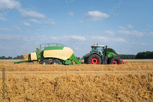 Strohernte - Traktor mit moderner Hochdruckpresse beim Pressen von Strohballen in Quaderform.