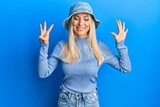 Young blonde woman wearing casual denim hat showing and pointing up with fingers number eight while smiling confident and happy.