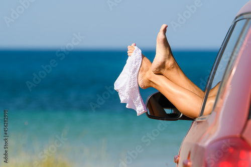 White swimsuit hangs on beautiful female legs from the car window on the background of the beach. The girl came to rest on a nudist beach. Nudist vacation concept photo