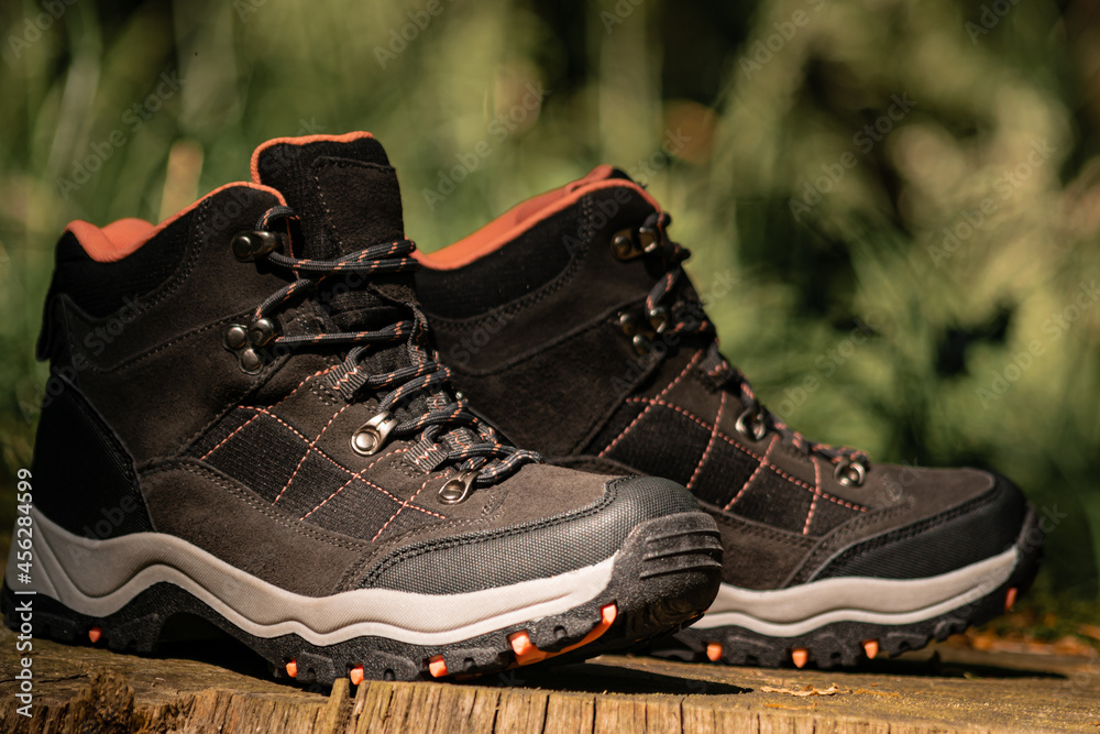 Closeup on pair of dark grey hiking boots on a natural raw wood in the woodland. Selective focus on dark shoes with ankle support for walking, surrounded by nature. Closeup on pair of dark grey hiking boots on a natural raw wood in the woodland. Selective focus on dark shoes with ankle support for walking, surrounded by nature.
