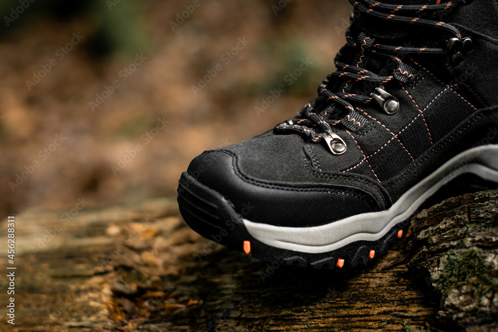 Closeup for dark grey single hiking boot on a natural raw wood in the woodland. Selective focus on one shoe standing on a wodden textured surface in the sun.
