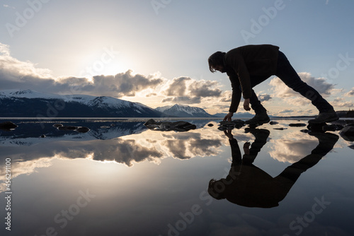 Unique view of a person with reflection in a natural lake with clouds and mountains in background. Awesome perspective of person. 