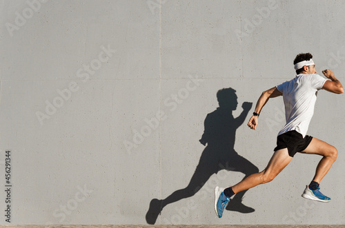 Caucasian young man doing sport jumping, shadow cast on the wall