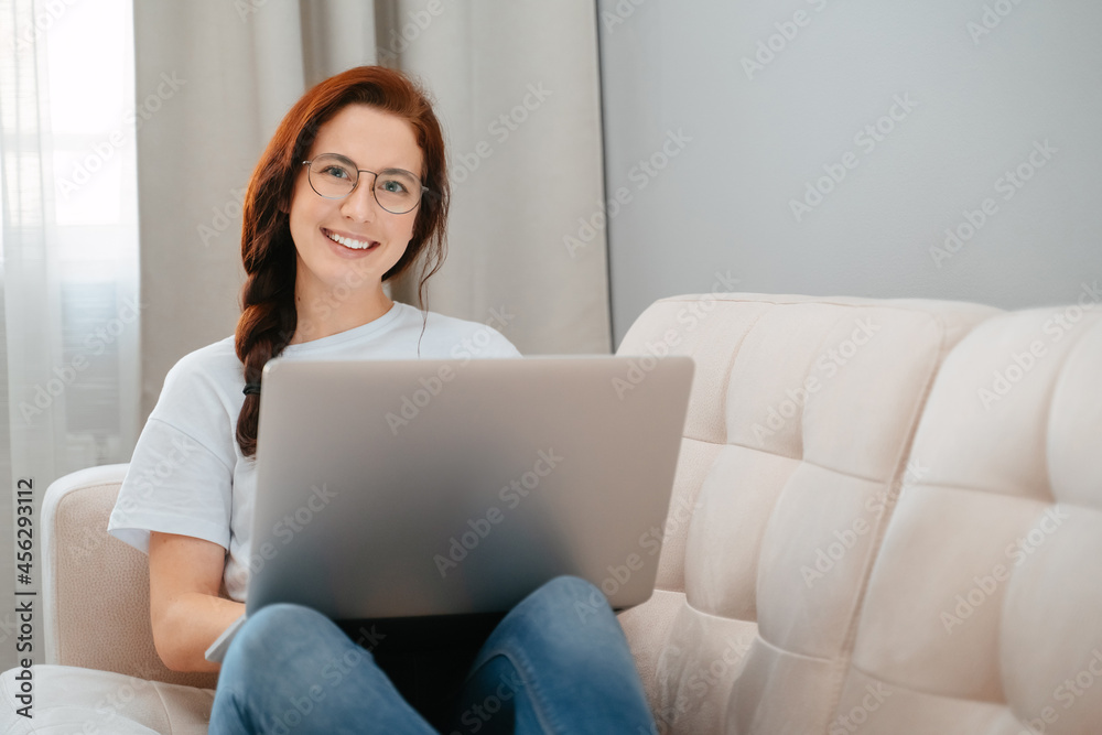 Young girl learns at home on a laptop sitting on a beige couch. The concept blogging and online work. Young girl learns at home on a laptop sitting on a beige couch. The concept blogging and online work.
