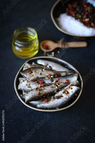 Sprat with spices in a plate on a dark background.
