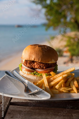 Large hamburger and chips served on a cafe table with sea views. Vacation and fast food