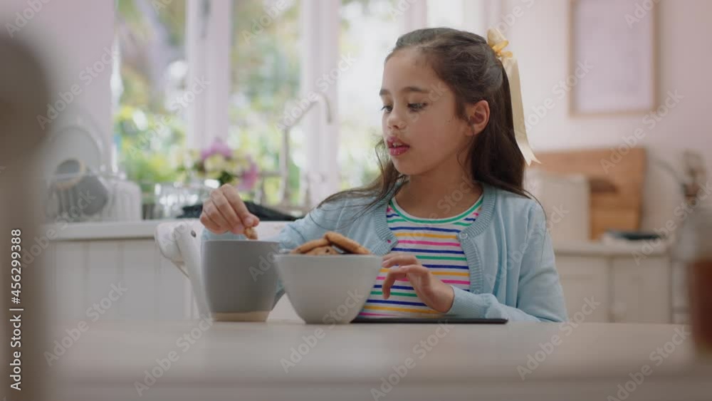 happy little girl using tablet computer eating cookie dipping biscuit into hot chocolate enjoying browsing online relaxing at home happy little girl using tablet computer eating cookie dipping biscuit into hot chocolate enjoying browsing online relaxing at home