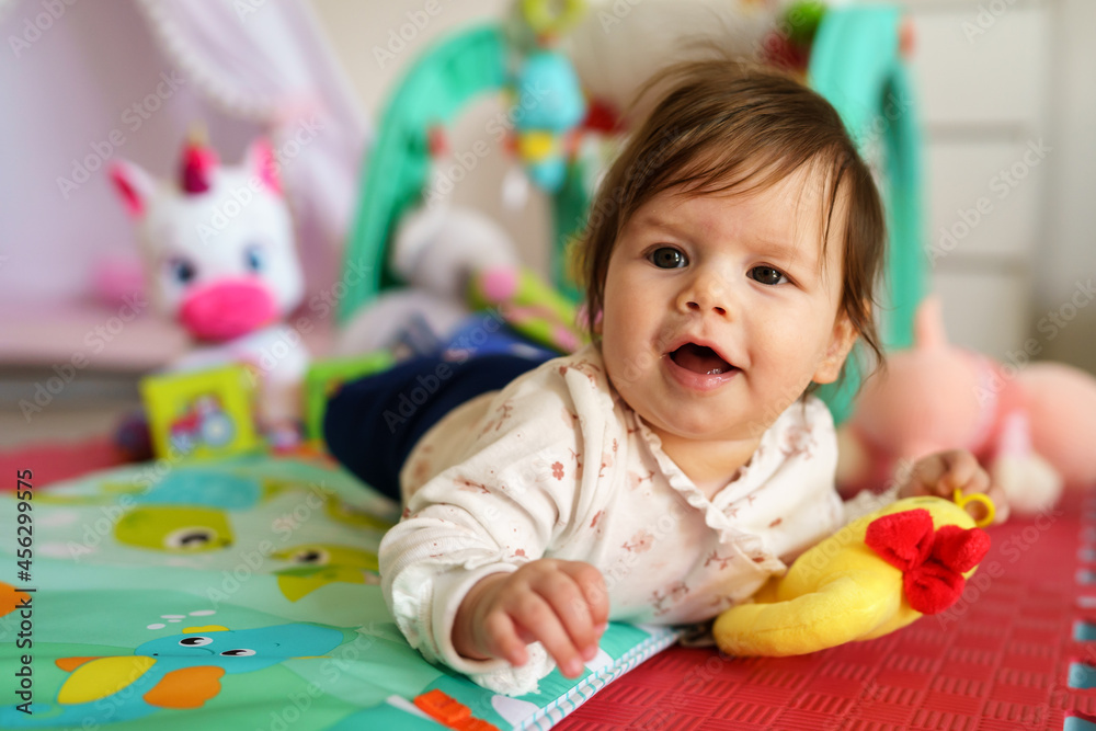 Close up on baby small caucasian girl five months old lying belly down on tummy at home in summer day playing with toy childhood concept looking to the side alone Close up on baby small caucasian girl five months old lying belly down on tummy at home in summer day playing with toy childhood concept looking to the side alone