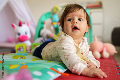 Close up on baby small caucasian girl five months old lying belly down on tummy at home in summer day playing with toy childhood concept looking to the side alone