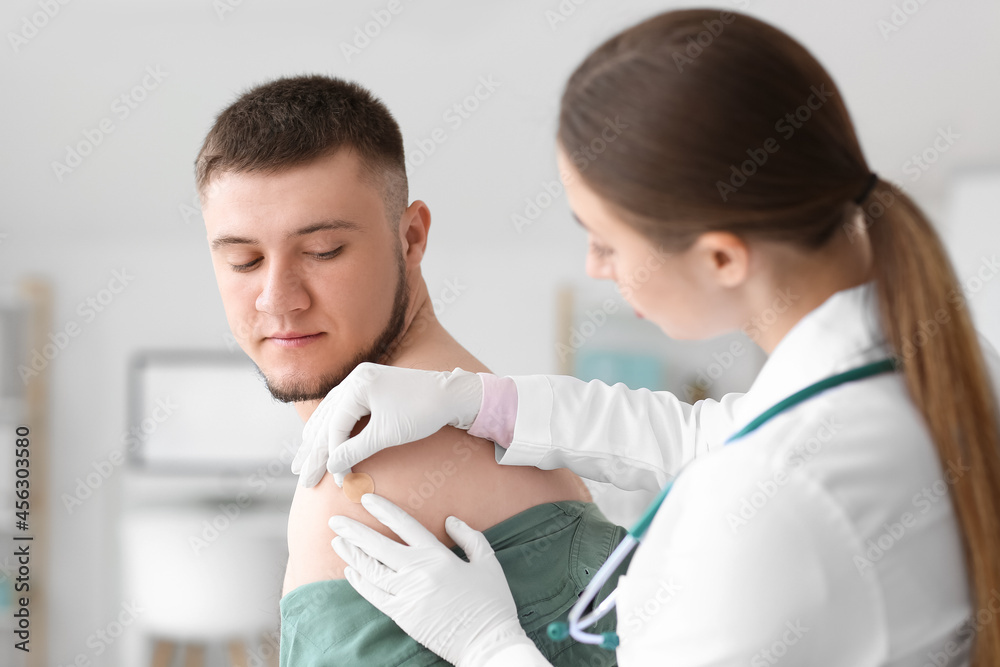 Doctor applying plaster onto shoulder of young man in clinic Doctor applying plaster onto shoulder of young man in clinic