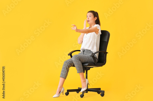 Fotografie Shocked young woman with imaginary steering wheel sitting in chair on color back