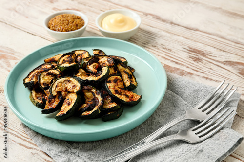 Plate with tasty grilled zucchini on light wooden background