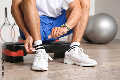 Sporty young man tying shoe laces in gym