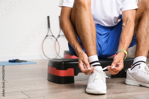 Sporty young man tying shoe laces in gym