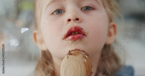 happy little girl licking spoon tasting delicious chocolate pudding enjoying homemade treats in kitchen 4k photo
