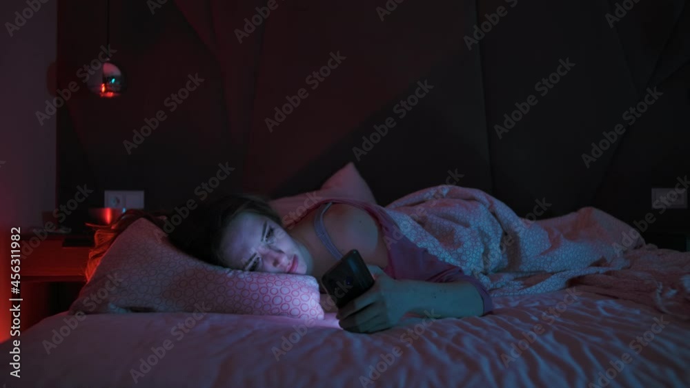 Young Woman have difficulty falling asleep Checking Mobile Phone A Young Woman Lies in Bed at Night and Cannot Sleep Insomnia a Sleep Disorder Concept Smartphone Addiction Young Woman have difficulty falling asleep Checking Mobile Phone A Young Woman Lies in Bed at Night and Cannot Sleep Insomnia a Sleep Disorder Concept Smartphone Addiction
